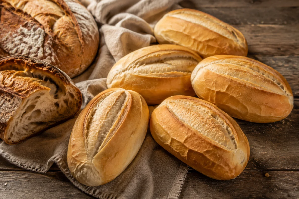 Pães franceses dourados e pães rústicos sobre uma mesa de madeira